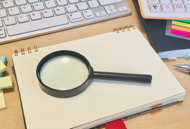 調査に必要なメモ帳、ペン、虫眼鏡、パソコンが映っている写真。